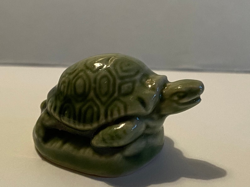 Pu&ograve; includere: Una statuetta di tartaruga in ceramica verde con un motivo a guscio dettagliato. La tartaruga &egrave; seduta su una base e ha la testa girata di lato.