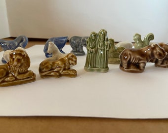 May include: A collection of ten small ceramic figurines, including a lion, a rooster, a goose, a hippopotamus, a donkey, a lamb, a woman, a man, a cat, and a horse. The figurines are all in various shades of brown, green, blue, and white.