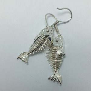May include: Silver fish skeleton earrings with a detailed design. The earrings are dangling and have a hook closure.