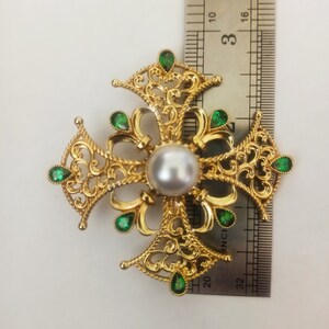 May include: A gold filigree cross with a white pearl in the center and green gemstones around the edges. The cross is about 3 inches wide.