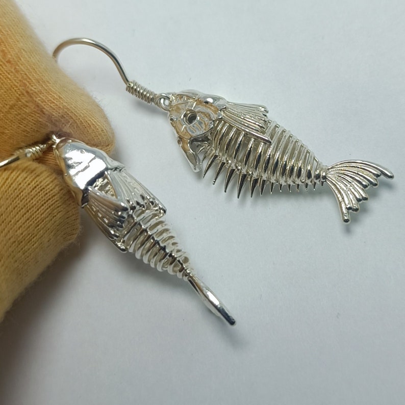 May include: A pair of silver fish skeleton earrings. The earrings are delicate and detailed, with a realistic fish skeleton design.