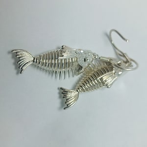 May include: Silver fish skeleton earrings with a detailed design. The earrings are dangling and have a hook closure.