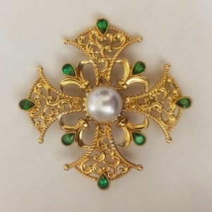 May include: A gold filigree cross pendant with a large white pearl in the center and green gemstones around the edges.