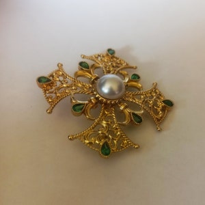 May include: A gold-tone cross pendant with a pearl center and green gem accents.