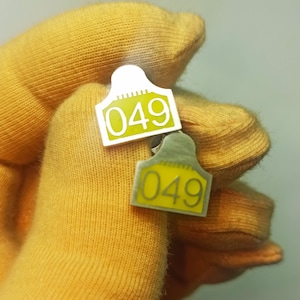 May include: Two silver metal tags with the number 049 printed in yellow on a yellow fabric background.