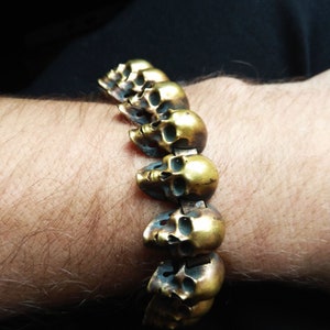 May include: A gold-toned bracelet made of linked skull charms. The bracelet is worn on a person's wrist.