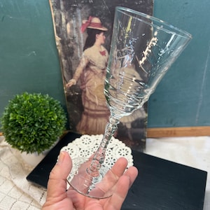 May include: A clear glass wine glass with a delicate etched design. The glass has a long stem and a round bowl.