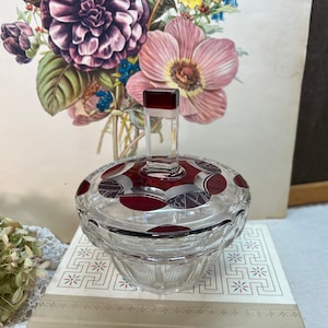 May include: A clear glass sugar bowl with a red and silver patterned lid. The lid has a red glass knob.