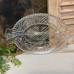 May include: A clear glass divided serving dish with a scalloped edge and a starburst pattern. The dish is divided into two sections.