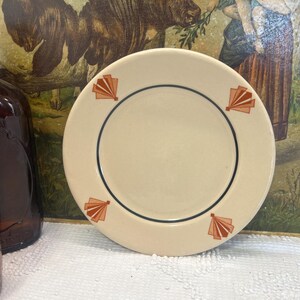May include: A cream-colored plate with a black border and orange fan-shaped designs. The plate is round and has a simple, elegant design. The plate is likely for serving food.