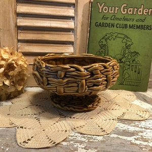 May include: A brown ceramic bowl with a woven design. The bowl has a pedestal base and is sitting on a crocheted doily.