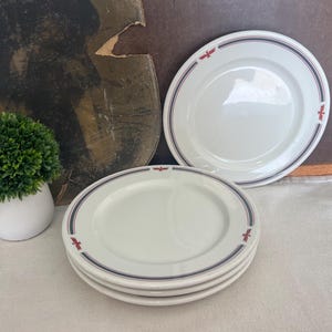 May include: Three white ceramic plates with a red and blue trim and a red eagle design. The plates are stacked on top of each other.