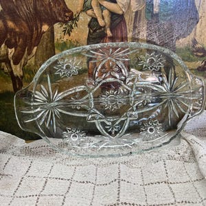 May include: A clear glass divided serving dish with a starburst pattern. The dish has two sections and is ideal for serving snacks or appetizers.