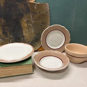 May include: A collection of vintage ceramic dishware in shades of white, tan, and brown. The set includes a small plate, a saucer, a bowl, and a teacup. The pieces have scalloped edges and a brown trim. The teacup has a handle.
