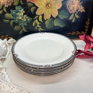 May include: A set of four white porcelain saucers with a silver trim and a delicate floral design. The saucers are stacked on top of each other.
