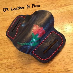 May include: A black leather knife sheath with red stitching and a painted red rose with green leaves.