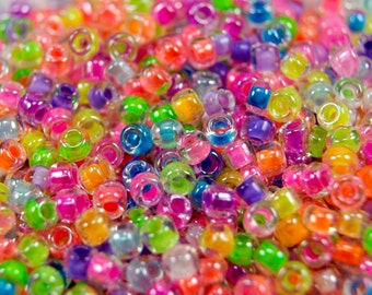 Op de afbeelding: Een close-up van een stapel kleurrijke, doorschijnende plastic kralen. De kralen zijn rond en hebben een gat in het midden. Ze zijn in een willekeurig patroon gerangschikt en zijn allemaal in verschillende kleuren, waaronder rood, oranje, geel, groen, blauw, paars en roze.