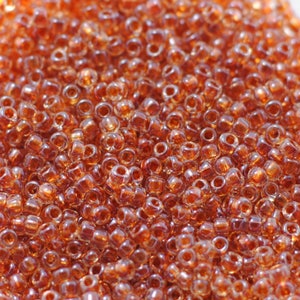 May include: A close-up image of a large quantity of small, round, transparent glass beads. The beads are a light amber color with a slight iridescent sheen.