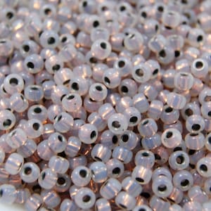 May include: A close-up of a pile of small, white, opaque glass beads with silver-toned metal caps. The beads have a slight iridescent sheen.