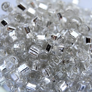May include: A close-up of a pile of clear plastic beads with silver accents. The beads are small and round, and they are perfect for crafting.