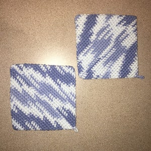 May include: Two crocheted pot holders in a blue and white color scheme. The pot holders are square shaped and have a diagonal pattern.
