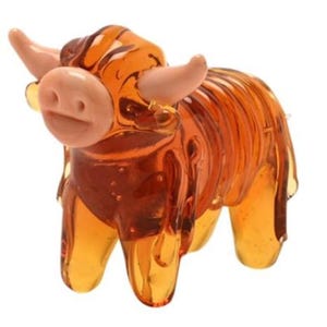 May include: A miniature, amber-hued glass Highland cow figurine. The cow features a light pink nose and horns, with a detailed, textured body. This decorative item is likely intended for display.
