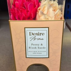 May include: A decorative box with a floral arrangement of pink and cream flowers. The box is labelled "Desire Aroma" and "Peony & Blush Suede". It is a hand-poured boutique diffuser.