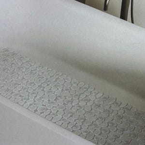 May include: A white bathtub with a clear, textured bath mat featuring a pebble design.