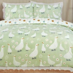 May include: A light green duvet cover and two pillowcases featuring a white goose pattern and small white flowers. The bedding set is made of a soft material and is designed for a bed. The duvet cover is approximately 203 cm wide.