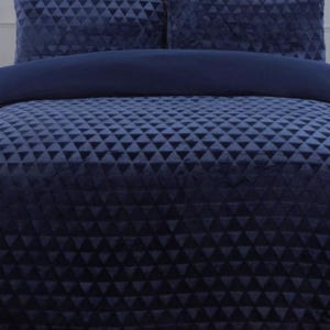 May include: A navy blue bed set, including a duvet cover and two pillowcases. The set has a repeating triangle pattern. The duvet cover is folded over the bed, and the pillowcases are propped up against the headboard. The set is made of a soft material.