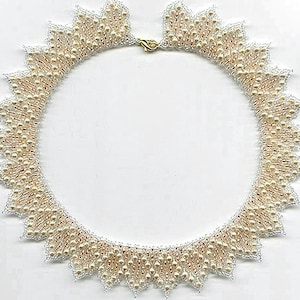 Op de afbeelding: Een witte en gouden kralenketting met een gegolfde rand. De ketting is gemaakt van kleine, ronde kralen en heeft een delicate, vrouwelijke uitstraling.