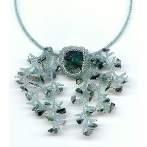 Könnte beinhalten: Eine handgefertigte Halskette mit einem zentralen, rechteckigen grünen Stein mit silberfarbenem Rand. Die Halskette hat einen hellblauen Perlenstrang und dekorative Perlenakzente mit kleinen, unregelmäßig geformten grünen und grauen Steinen.