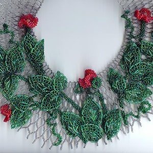 Puede incluir: Un collar de cuentas con una base de malla plateada y hojas verdes y flores rojas.