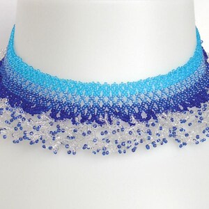 May include: A blue and white beaded choker necklace with a graduated ombre effect. The necklace has a delicate, lacy fringe.