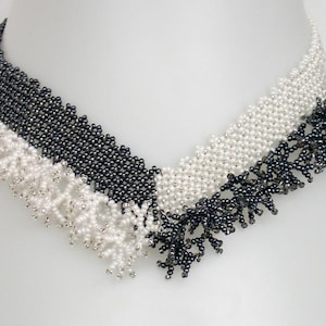May include: A black, white, and silver beaded necklace with a geometric design. The necklace is made of small, round beads that are strung together in a pattern of triangles and squares. The necklace is finished with a delicate fringe of beads.