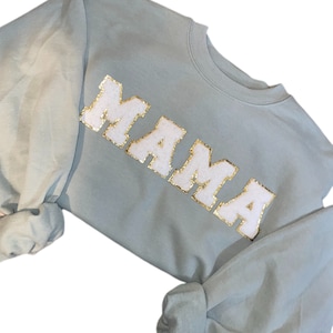 May include: Light blue sweatshirt with the word "MAMA" in white fuzzy letters with gold glitter outlining.