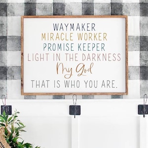 Könnte beinhalten: Ein Holzschild mit dem Text "WAYMAKER MIRACLE WORKER PROMISE KEEPER LIGHT IN THE DARKNESS My God THAT IS WHO YOU ARE." Das Schild hängt an einer Wand mit schwarz-weiß kariertem Tapetenmuster.