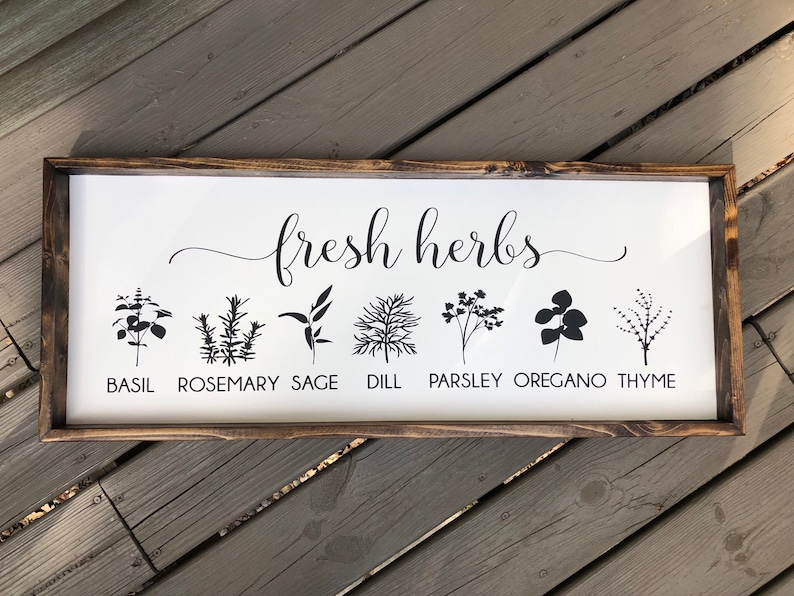 May include: A white wooden sign with the text "fresh herbs" in black cursive script.  The sign features black silhouettes of various herbs, including basil, rosemary, sage, dill, parsley, oregano, and thyme, with the name of each herb printed below.