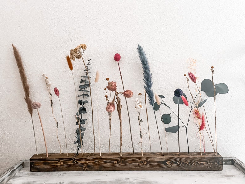 Pu&ograve; includere: Un supporto in legno con 15 fori per fiori secchi e verde. Il supporto &egrave; marrone scuro e ha una finitura rustica. I fiori includono erba della pampa secca, eucalipto e vari altri fiori secchi in tonalit&agrave; di rosa, rosso e bianco.