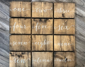 May include: Twelve wooden signs with white calligraphy, each displaying a number from one to twelve. The signs are arranged in three rows of four, with the numbers increasing from left to right and top to bottom.