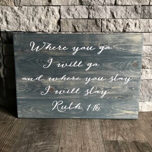 May include: A wooden sign with a gray stain and white lettering. The sign reads "Where you go I will go and where you stay I will stay Ruth 1:16".