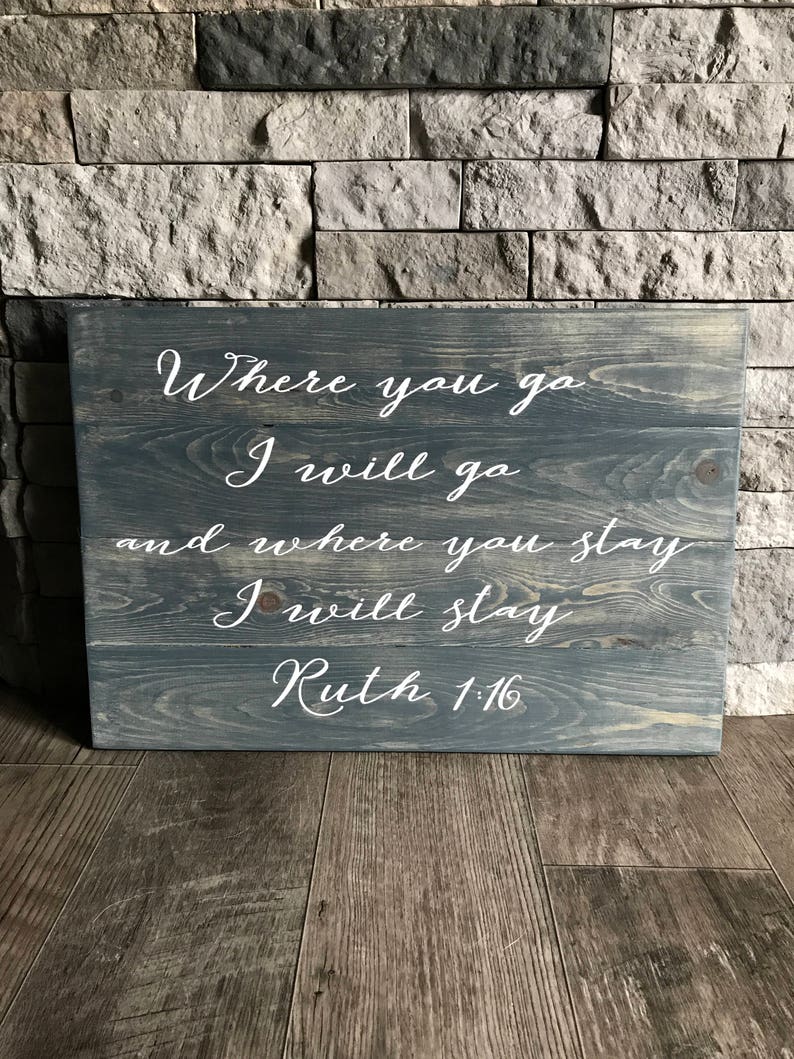 May include: A wooden sign with a gray stain and white lettering. The sign reads "Where you go I will go and where you stay I will stay Ruth 1:16".