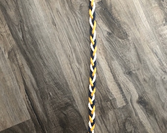 May include: A long, braided rope with black, white, and gold strands. The rope is tied with a brown bow at the end.
