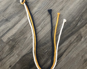 May include: Three strands of rope, one white, one yellow, and one black, are tied together with a silver ring at the top.
