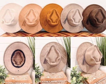 Peut inclure: Plusieurs chapeaux à larges bords de couleurs neutres, crème, beige et marron. Chaque chapeau a une couronne structurée, une décoration en forme de gland et un large bord. Les chapeaux sont présentés sur une surface en bois et sur fond blanc.