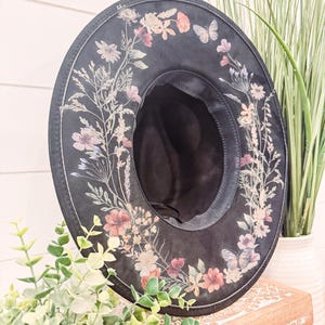 May include: A black wide-brimmed hat with a floral print design. The hat has a black band around the crown and a black ribbon tied around the brim.