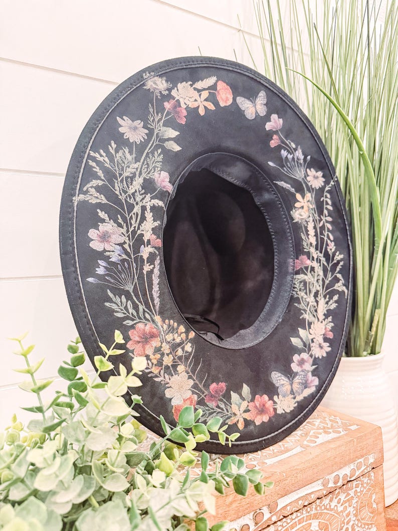 May include: A black wide-brimmed hat with a floral print design. The hat has a black band around the crown and a black ribbon tied around the brim.