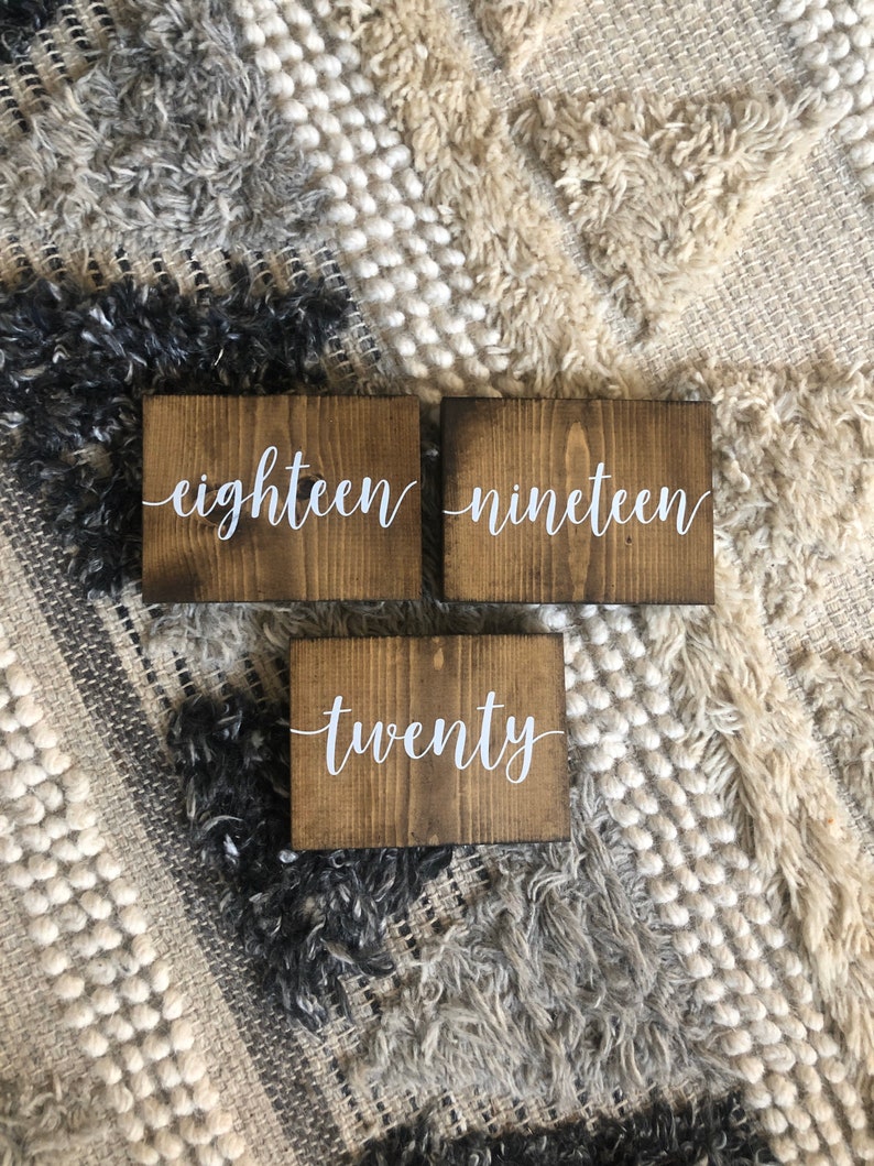 May include: Three wooden signs with white lettering. The signs read "eighteen", "nineteen", and "twenty".