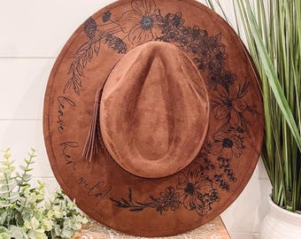 May include: A brown suede hat with a black floral design and the text "Let her run wild".