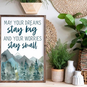 Può includere: Una stampa incorniciata con un'illustrazione ad acquerello di montagne e alberi. La stampa ha il testo "Che i tuoi sogni restino grandi e le tue preoccupazioni restino piccole".